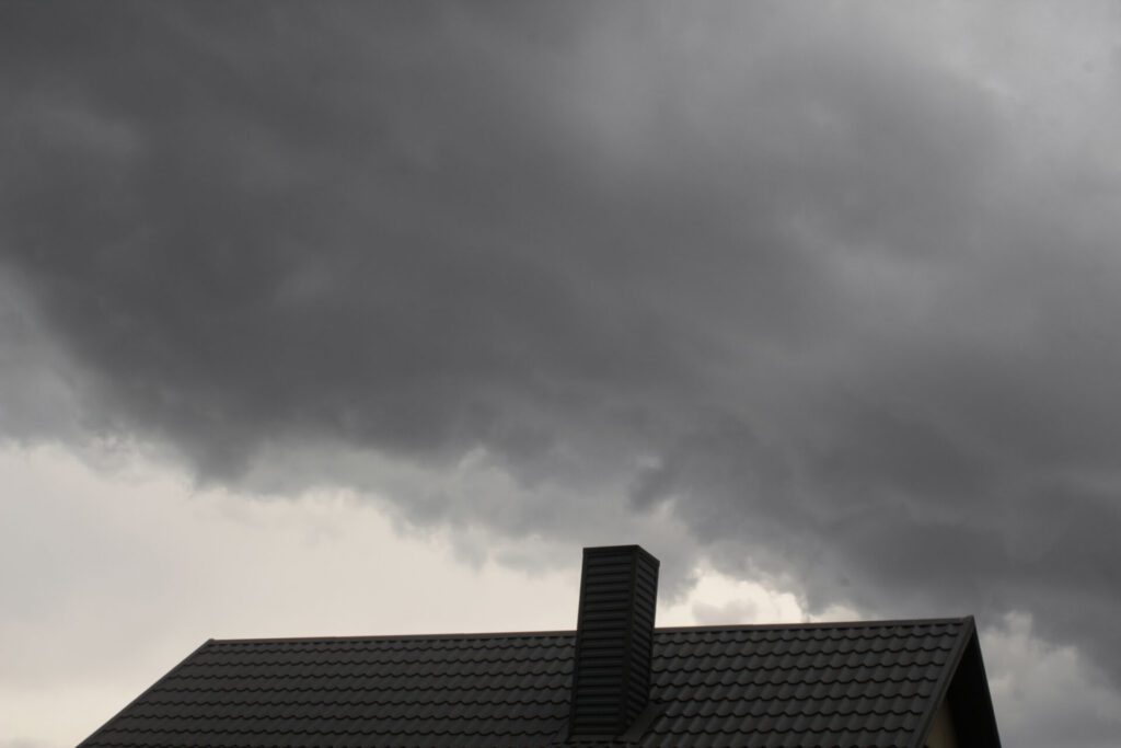 Dark storm clouds over a commercial metal roof, emphasizing the need for storm preparation and roof inspections. - Storm Damage Repair