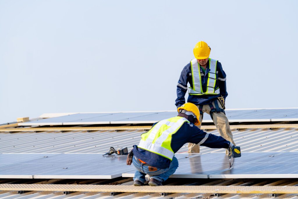Workers installing solar panels on a commercial metal roof to enhance energy-efficient roofing and lower utility bills for businesses.
