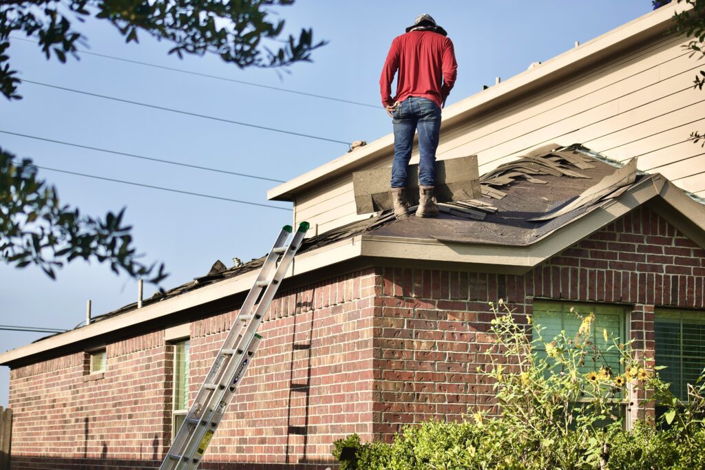 Roofer inspecting damaged asphalt shingles on a residential roof in West Texas, preparing for roof repair or installation after storm damage.