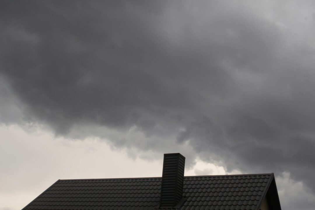 Dark storm clouds over a commercial metal roof, emphasizing the need for storm preparation and roof inspections. - Storm Damage Repair